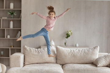 Portrait of smiling small teen biracial girl child jump on couch in living room relax alone in new...