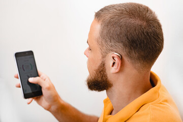 Hearing impaired man adjusts settings for his BTE hearing aid via smartphone. Hearing aids, deafness treatment, innovative technologies at audiology
