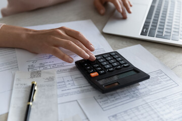 Crop close up of female sit at desk calculate expenses expenditures on machine pay bills taxes...