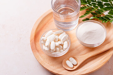 Collagen powder, pills and glass of water on wooden tray, top view