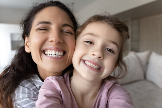 Close Up Portrait Of Overjoyed Young Latino Mother And Little Biracial Daughter Make Selfie Together. Happy Hispanic Mom And Small Ethic Girl Child Take Self-portrait Picture On Camera At Home.