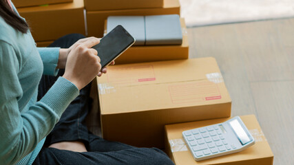 Asian young woman SME business owner with online shopping working on laptop computer with parcel box on shop table - SME online business idea and delivery