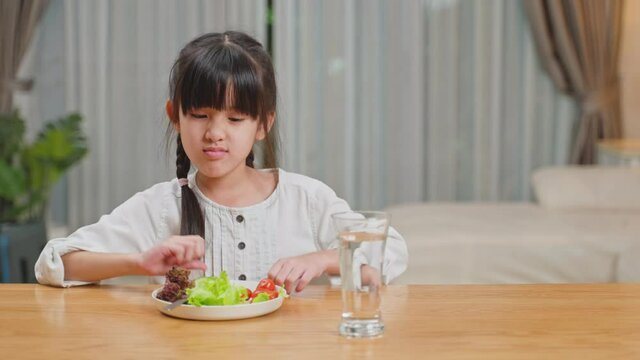 Unhappy Asian girl don't want to eat green vegetables on dinner plate.