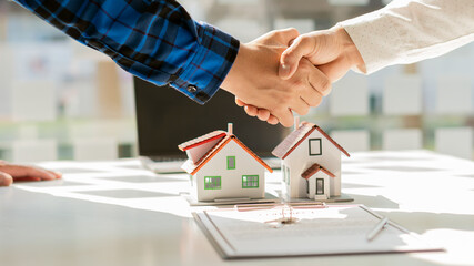 Real estate agents shake hands with prospective clients to buy a documented home in the office. and offer a house model for customers to buy with insurance