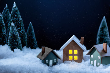 New year and Christmas background. There are artificial  christmas trees, three figurines of wooden houses and artificial snow on the photography. Copy space. Horizontal orientation.