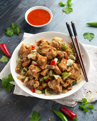 Stir fry chinese salt and pepper chicken with red, green chilli, onion, spring onion in white bowl.