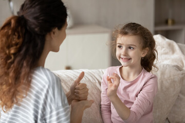 Hispanic mother and small ethnic daughter talk communicate using hand gestures. Cute little teen biracial disabled kid child practice speak with sign language with mom or coach. Nonverbal concept.