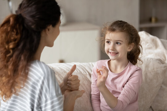 Hispanic Mother And Small Ethnic Daughter Talk Communicate Using Hand Gestures. Cute Little Teen Biracial Disabled Kid Child Practice Speak With Sign Language With Mom Or Coach. Nonverbal Concept.