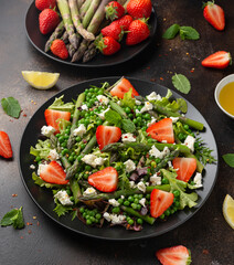 Asparagus and Strawberry Salad with vegetables, green peas and feta cheese in black plate. healthy food.