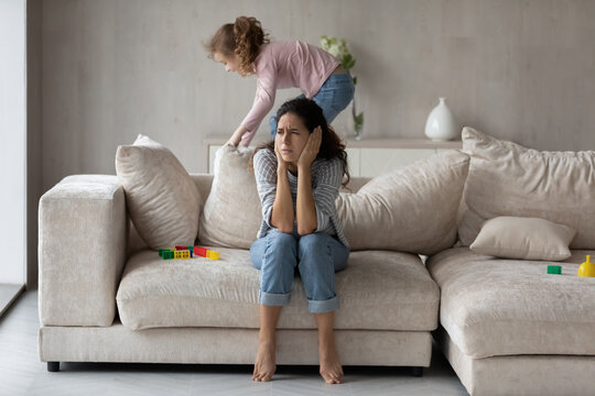 Exhausted Hispanic young mother bothered by loud noise biracial teen daughter playing at home. Tired Latin mom annoyed by ill-behaved naughty kid, suffer from headache. Parenthood concept.