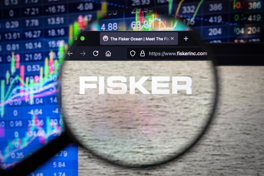 Fisker company logo on a website with blurry stock market developments in the background, seen on a computer screen through a magnifying glass