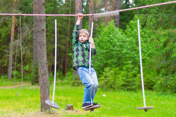 A boy overcomes obstacles in a rope track in the forest in summer or spring