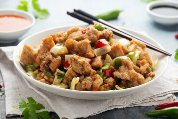 Stir fry chinese salt and pepper chicken with red, green chilli, onion, spring onion in white bowl.