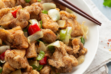 Stir fry chinese salt and pepper chicken with red, green chilli, onion, spring onion in white bowl.
