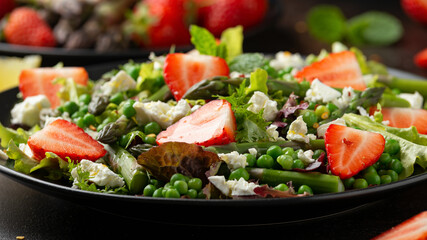 Asparagus and Strawberry Salad with vegetables, green peas and feta cheese in black plate. healthy food.