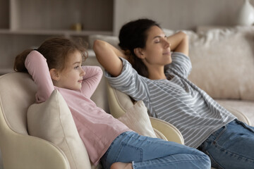Calm happy young Latino mother and little teen daughter relax on sofa in living room relieve negative emotions. Hispanic mom and teenage girl child rest together on couch take nap or sleep.