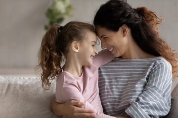 Happy young Hispanic mother and small teen ethnic daughter touch foreheads enjoy tender close family moment together. Smiling Latin mom and little biracial girl child hug show love and care.