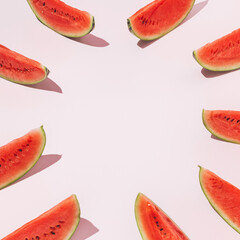 Minimal frame with slices of juicy and ripe watermelon ordered in a circle isolated on a pastel pink background. Creative summer fruit food concept with copy space. Flat lay, top view.