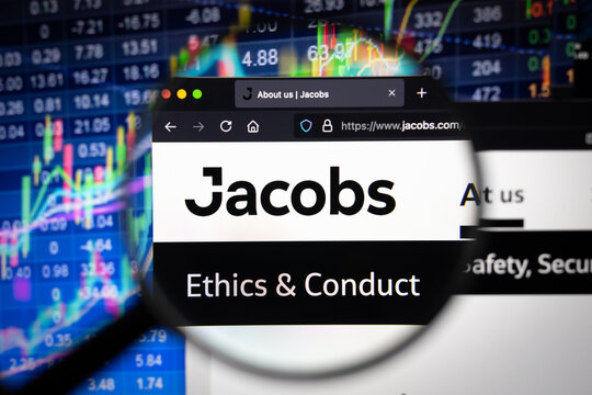 Jacobs company logo on a website with blurry stock market developments in the background, seen on a computer screen through a magnifying glass