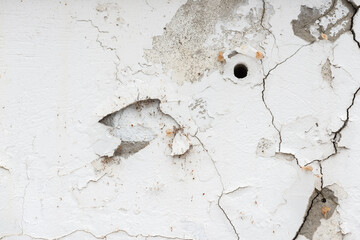 peeling paint on a wall with cracking or fracture lines and a round hole
