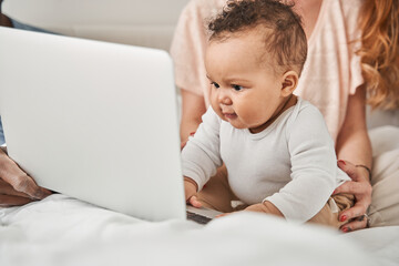 Baby sitting at the bed and looking at the laptop with interest