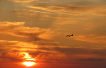 Airplane flies against the orange-gold sunset background
