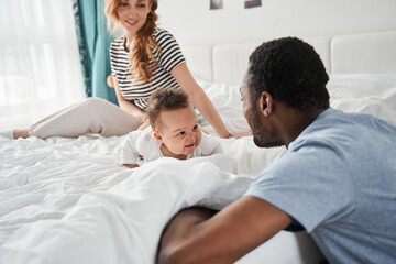 Family having fun with their kid on the bed while playing