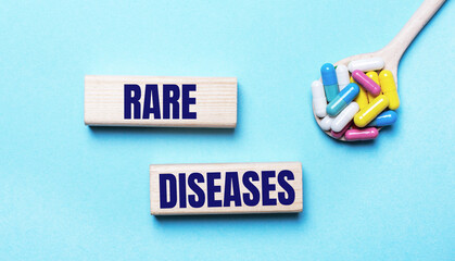 On a light blue background, bright multi-colored pills in a spoon and two wooden blocks with the text RARE DISEASES. Medical concept