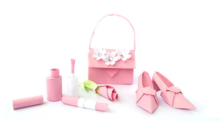 Origami paper background with shoes, bag, lipstick, nail polish and flowers. Handmade pink high heels isolated on white background. Origami composition. Paper craft. 