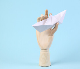 Wooden hand holds origami paper boat on blue background