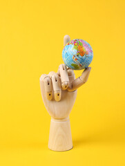 Wooden hand holding globe on yellow background