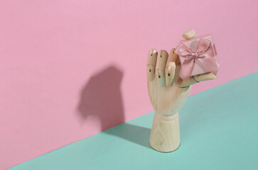 Wooden hand holding gift box on blue pink pastel background. Trendy shadow. Concept art. Minimalism. Creative layout
