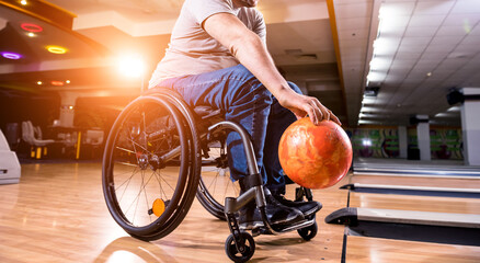 Young disabled man in wheelchair playing bowling in the club