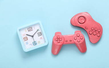 Two pink gamepads with alarm clock on blue background. Time to play video games