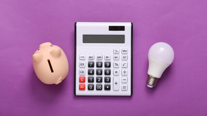 Calculator and piggy bank, light bulb on purple background. Top view