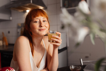 Woman holding glass of orange juice and coquettish looking at the camera