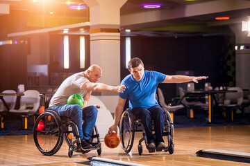 Two young disabled men in wheelchairs playing bowling in the club
