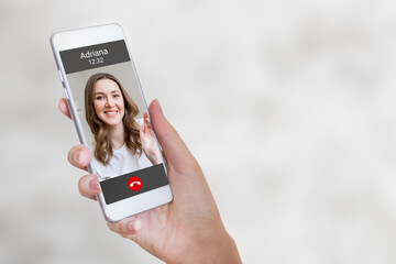 A female hand holds a mobile phone with a girl on the screen, video chat. A woman makes a video...
