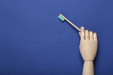 Wooden hand holds bamboo eco toothbrush on blue background