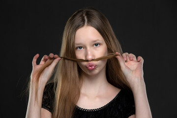 Beautiful teenage girl fooling around in front of the camera. She makes a mustache out of her hair.