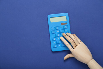 Wooden hand uses a calculator on blue background