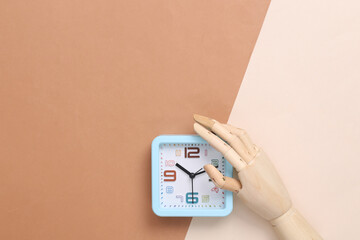 Wooden hand holds alarm clock on brown-beige background