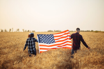 Back view of a happy family in wheat field with USA, american flag. The concept of freedom. US flag. 4th of July. Independence Day.