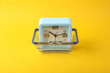 Clock with a shopping basket on a yellow background. Shopping time