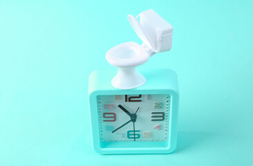 Alarm clock and mini toilet on a blue background. Incorrect timing