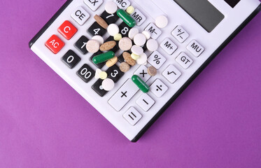 Pills and calculator on purple background.