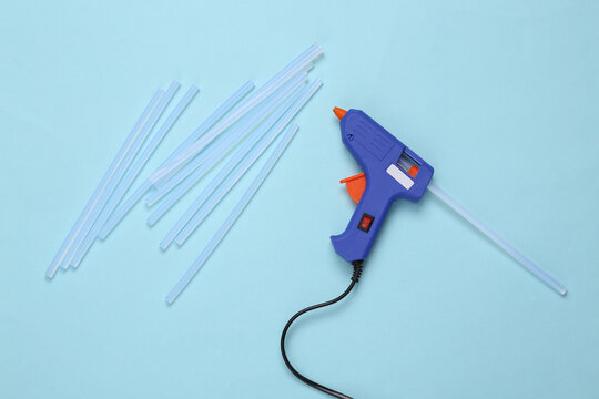 Glue gun with glue stick on blue background.