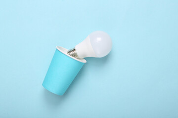 Cardboard cup with light bulb on blue background.