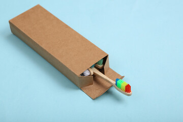 Rainbow toothbrush in cardboard box on blue background.