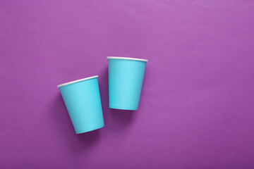Empty blue cardboard coffee cups on purple background. Minimalism